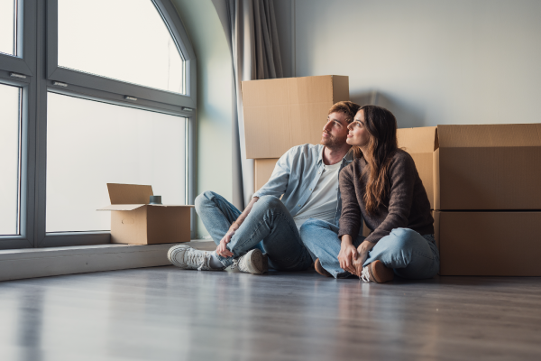 A couple looking out of the window of their new home sitting in front of moving boxes.